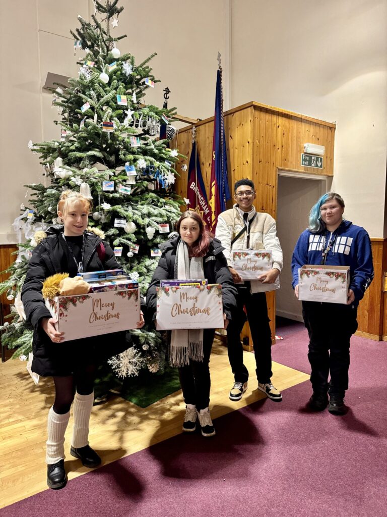 Four Cadbury students stand in front of the Christmas tree with their donations