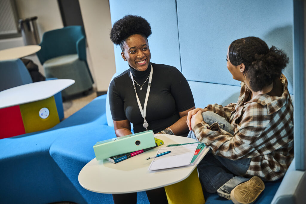 Lecturer sitting at table smiling at student