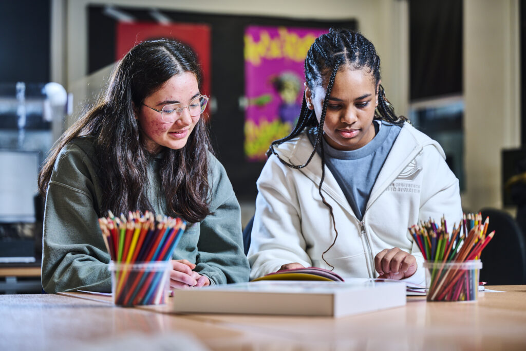 Two students in a classroom reading a book