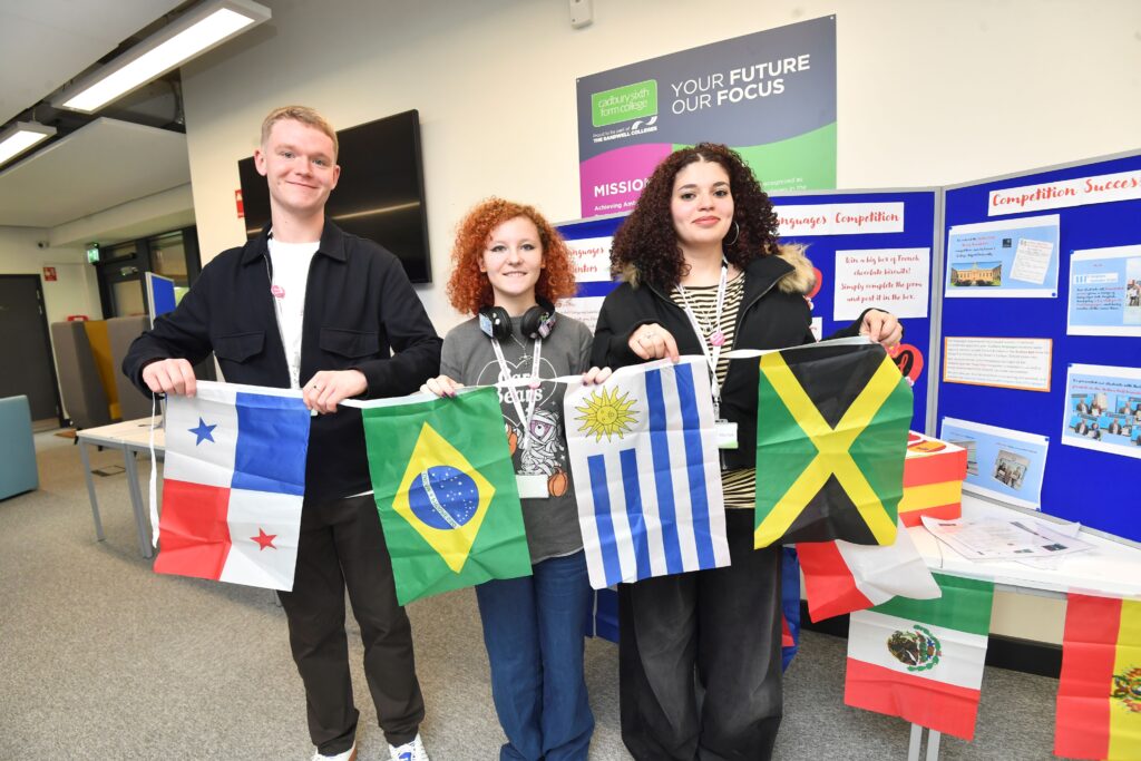 Three language alumni stand holding flags from around the world